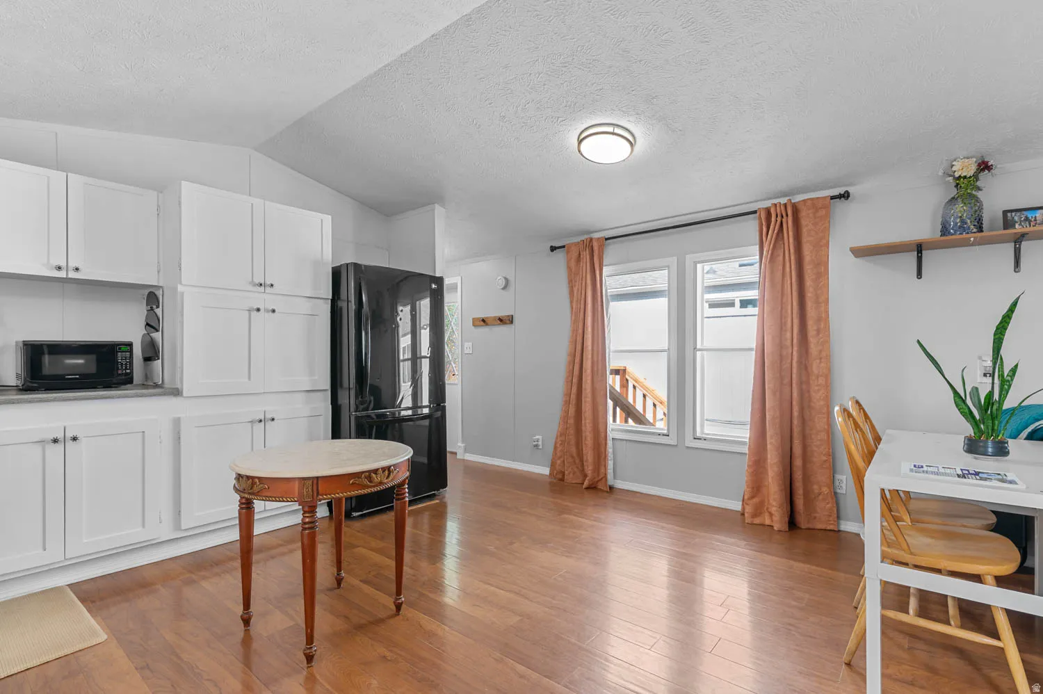 Open-concept living space with wood-finish flooring, white cabinetry, and a black refrigerator