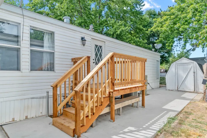 Rear exterior featuring a natural wood deck with railings, a white shed, concrete patio, and mature trees