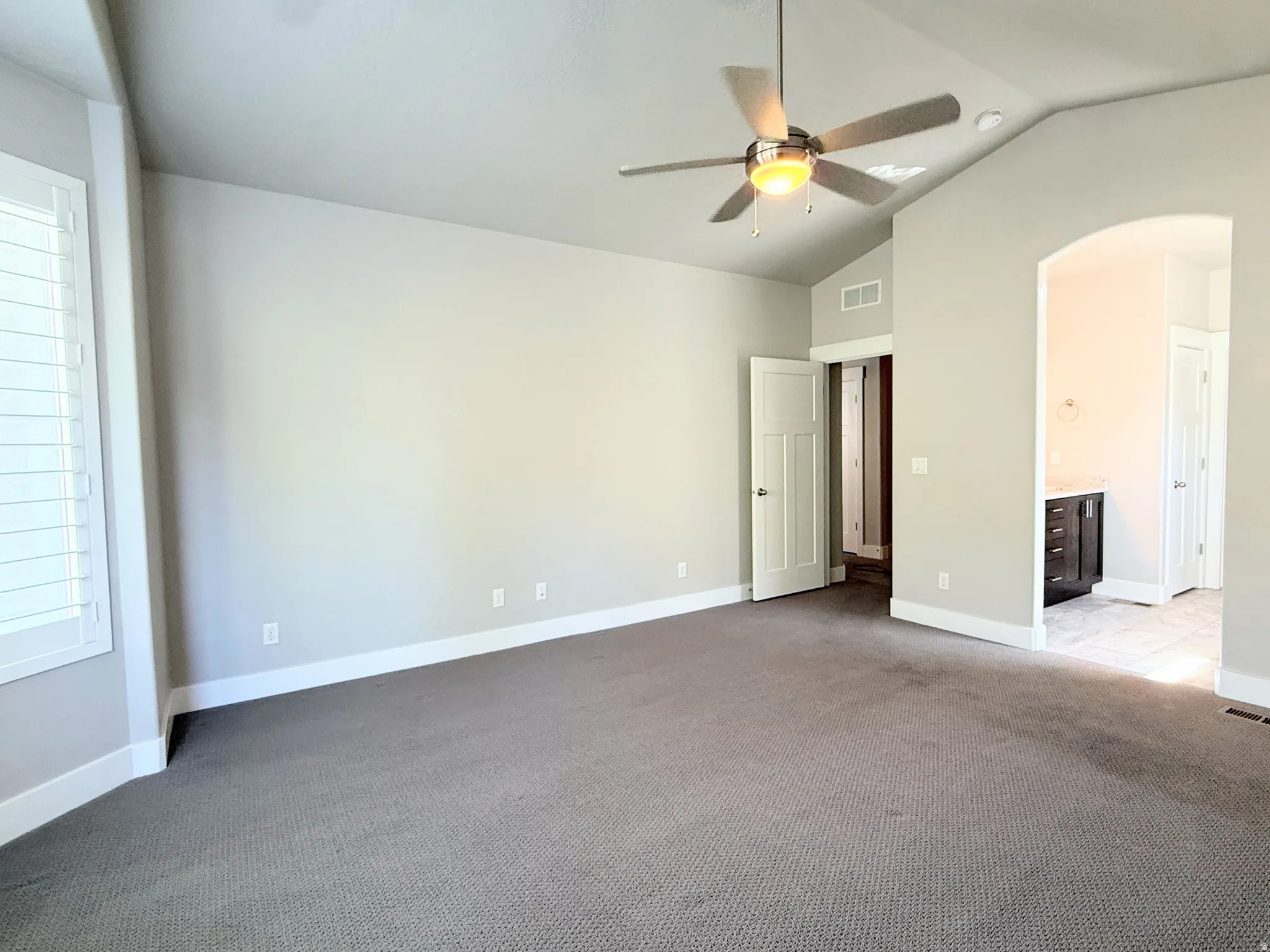 Spacious Primary Bedroom featuring vaulted ceilings, a ceiling fan with integrated lighting, plantation shutters, and soft gray carpeting
