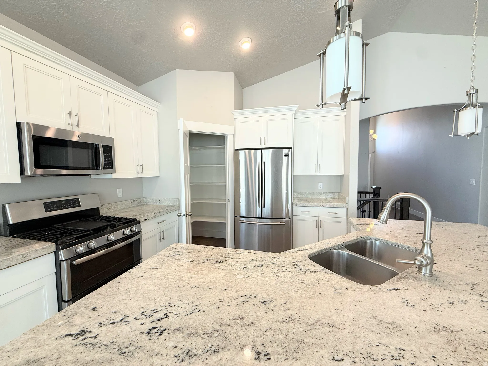 Kitchen featuring light-toned granite countertops, stainless steel appliances, white cabinetry, a double basin sink with a gooseneck faucet, and recessed lighting