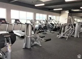 Community fitness center featuring multiple cardio machines, weight training equipment, large windows, recessed lighting, and rubber flooring