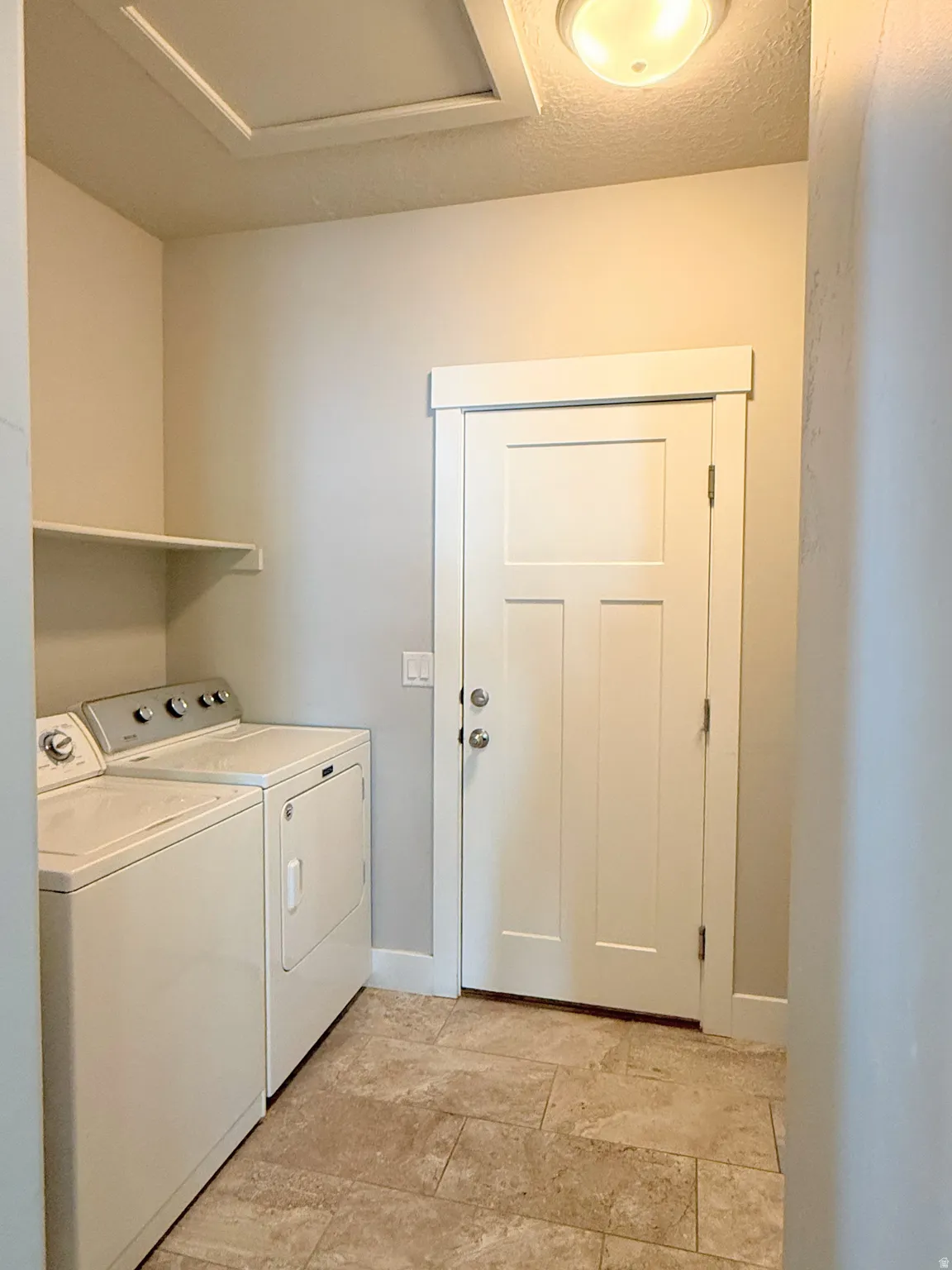 Laundry area featuring stone-look tile flooring, a built-in wall shelf, and a panel door to the garage with contemporary trim