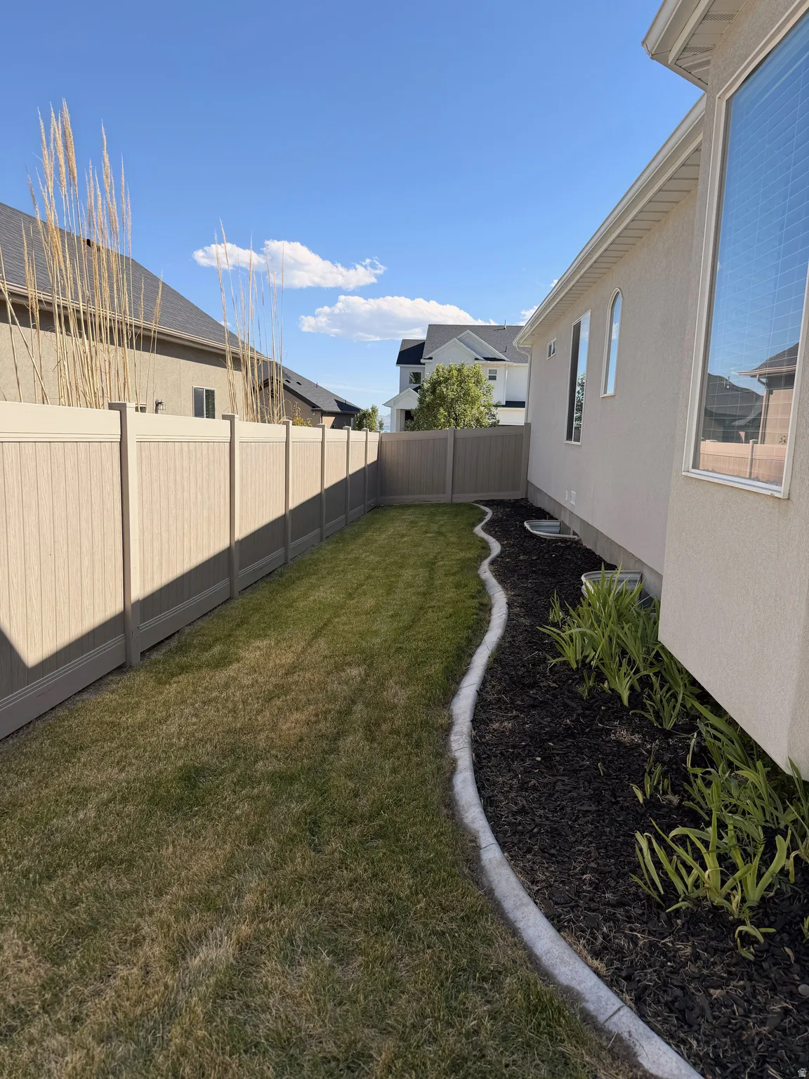 Private backyard with a manicured lawn, established landscaping, and durable fencing