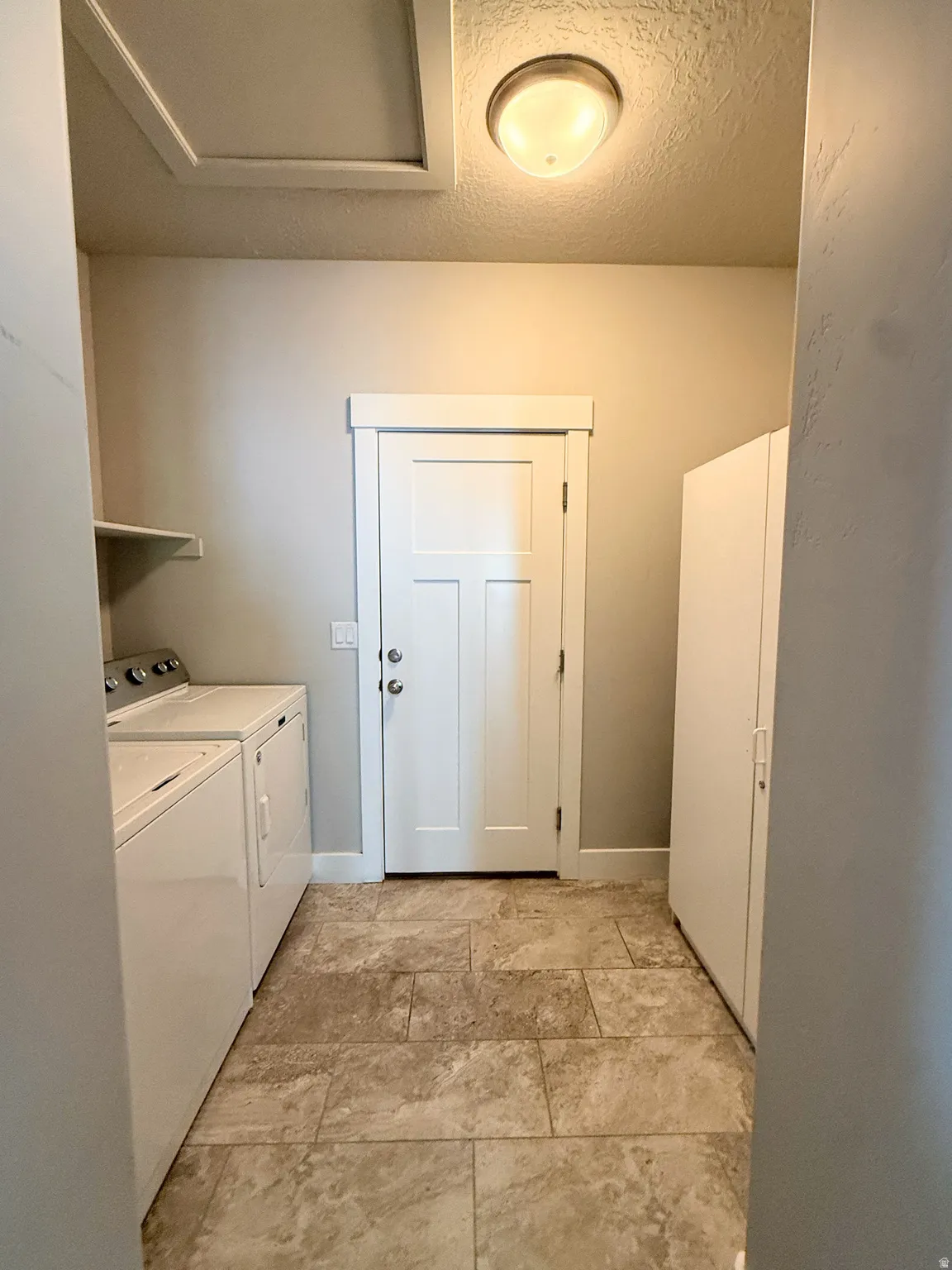 Laundry area featuring a side-by-side washer and dryer, tile flooring, and a white paneled door to the garage with brushed nickel hardware