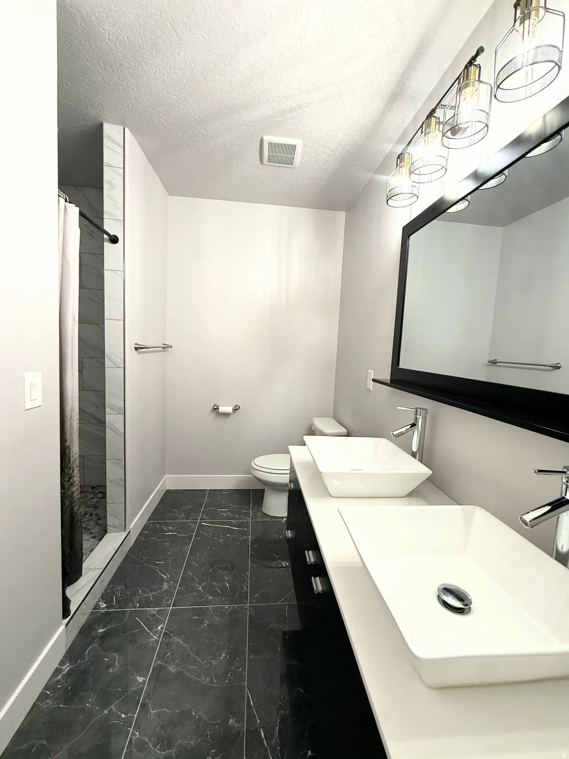 Basement Bathroom #3 featuring walk in shower, dual vessel sinks with chrome faucets, a dark vanity, and a large wall-mounted mirror with an overhead light fixture