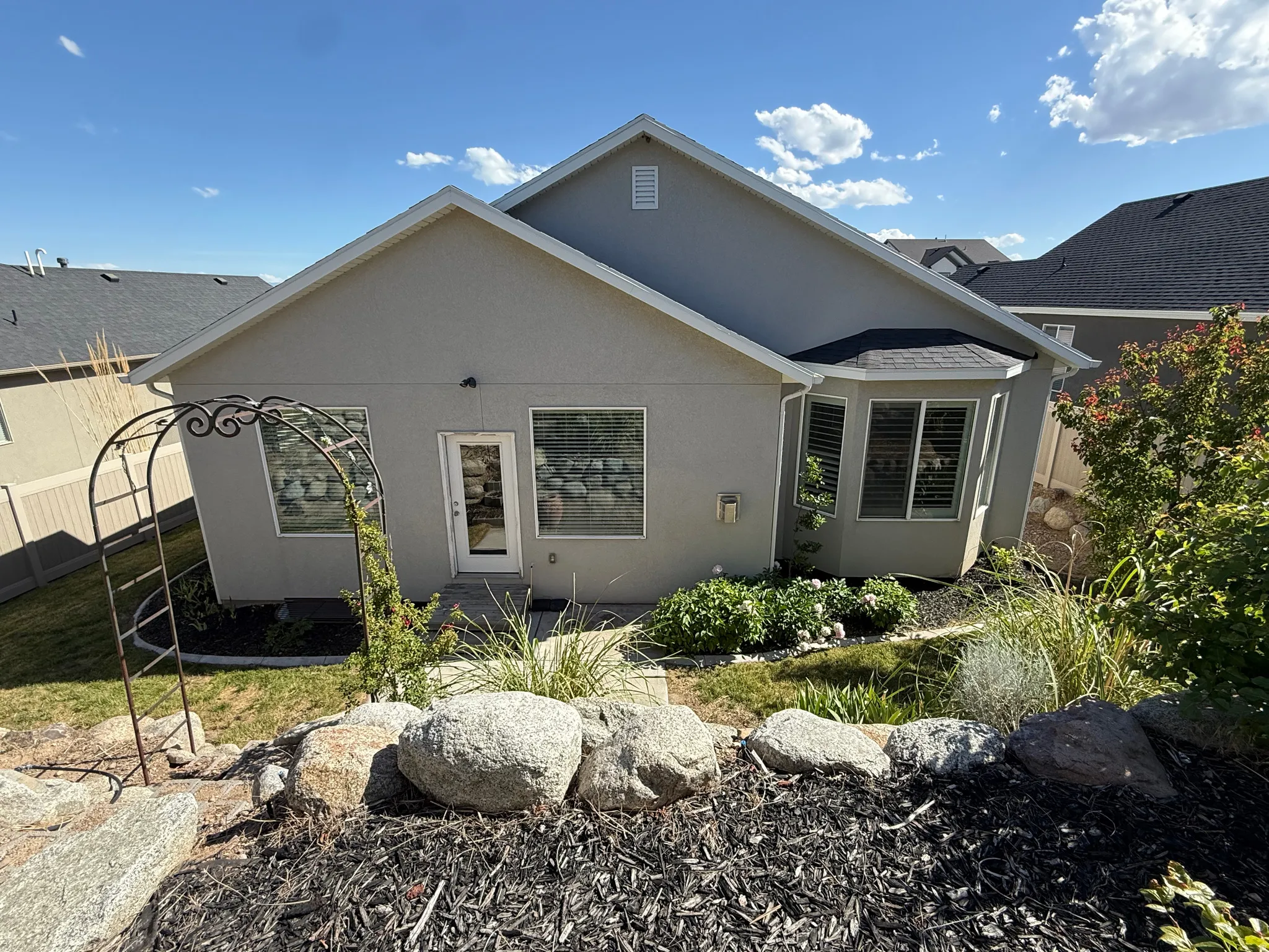 Rear exterior featuring a stucco facade, multiple windows, and a glass-paneled door, and and iron ornamental trellis garden arch.