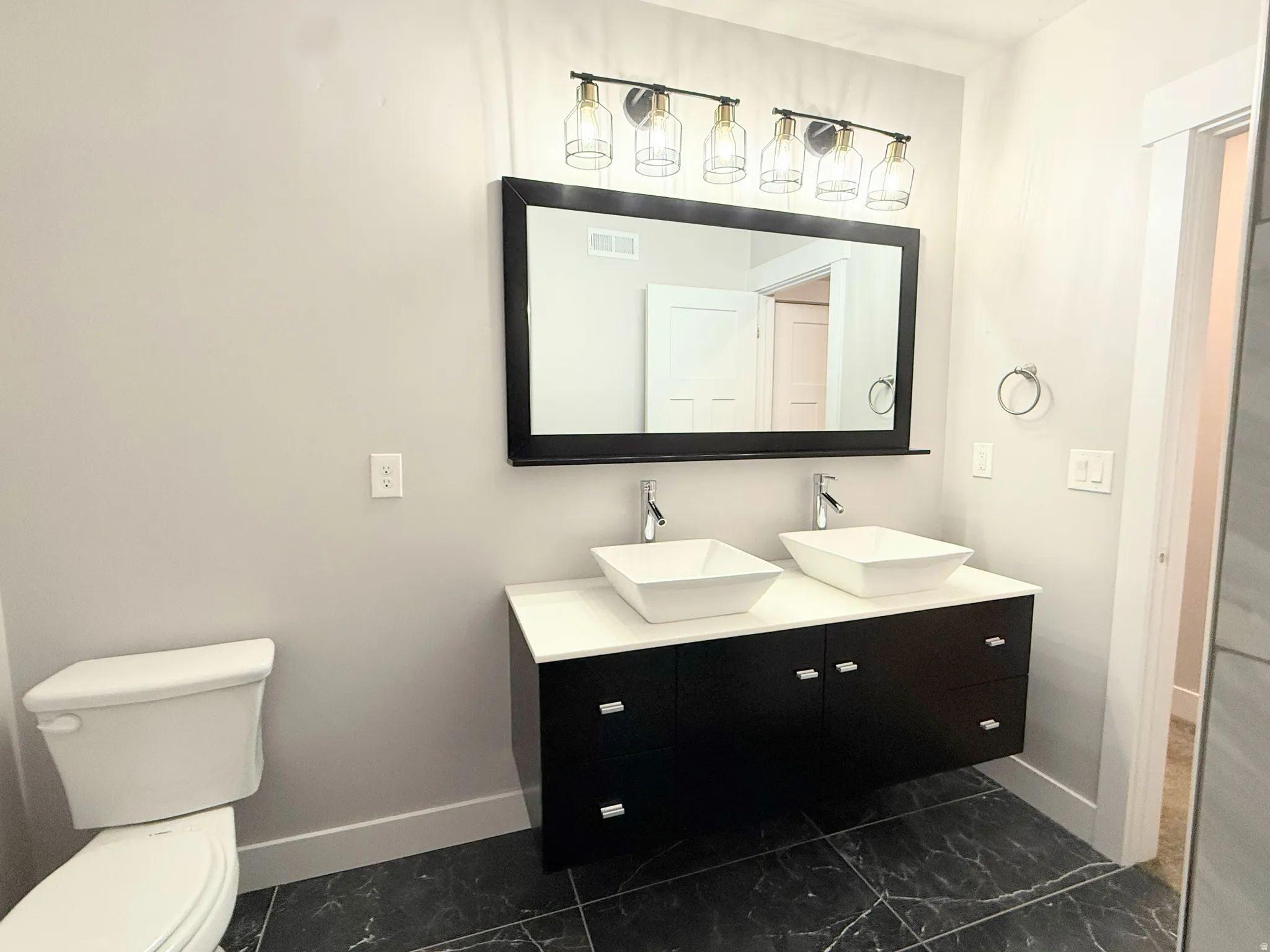 Bathroom featuring a black floating vanity with white countertops, dual vessel sinks, and matte black and gold-tone light fixture