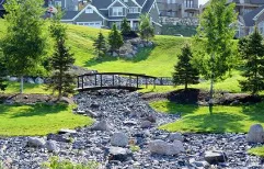 Community Park on a hillside featuring a pedestrian bridge over a rocky dry creek bed, surrounded by manicured lawns and mature trees
