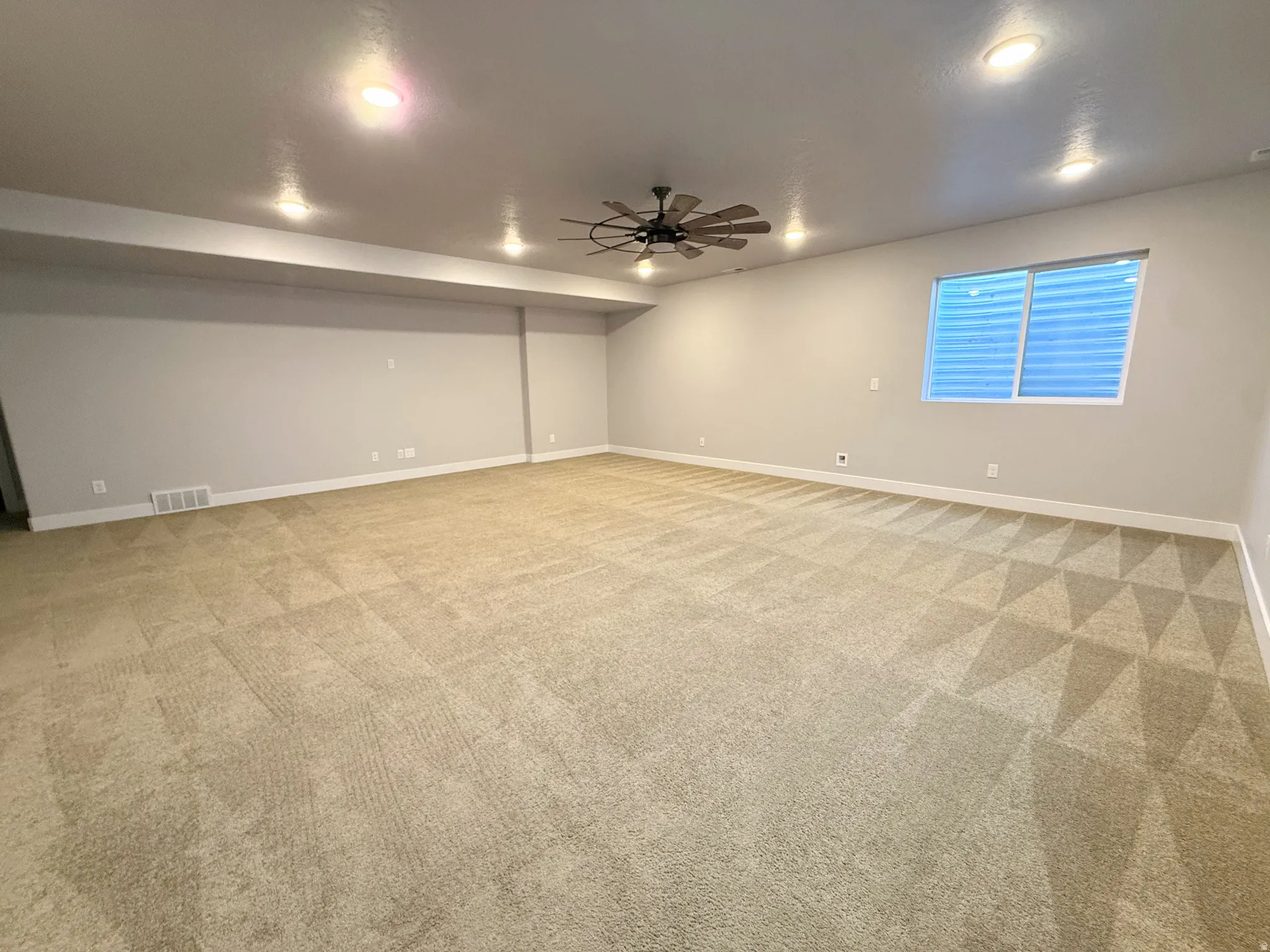 Expansive carpeted room featuring recessed lighting, a ceiling fan, and a windows with blinds