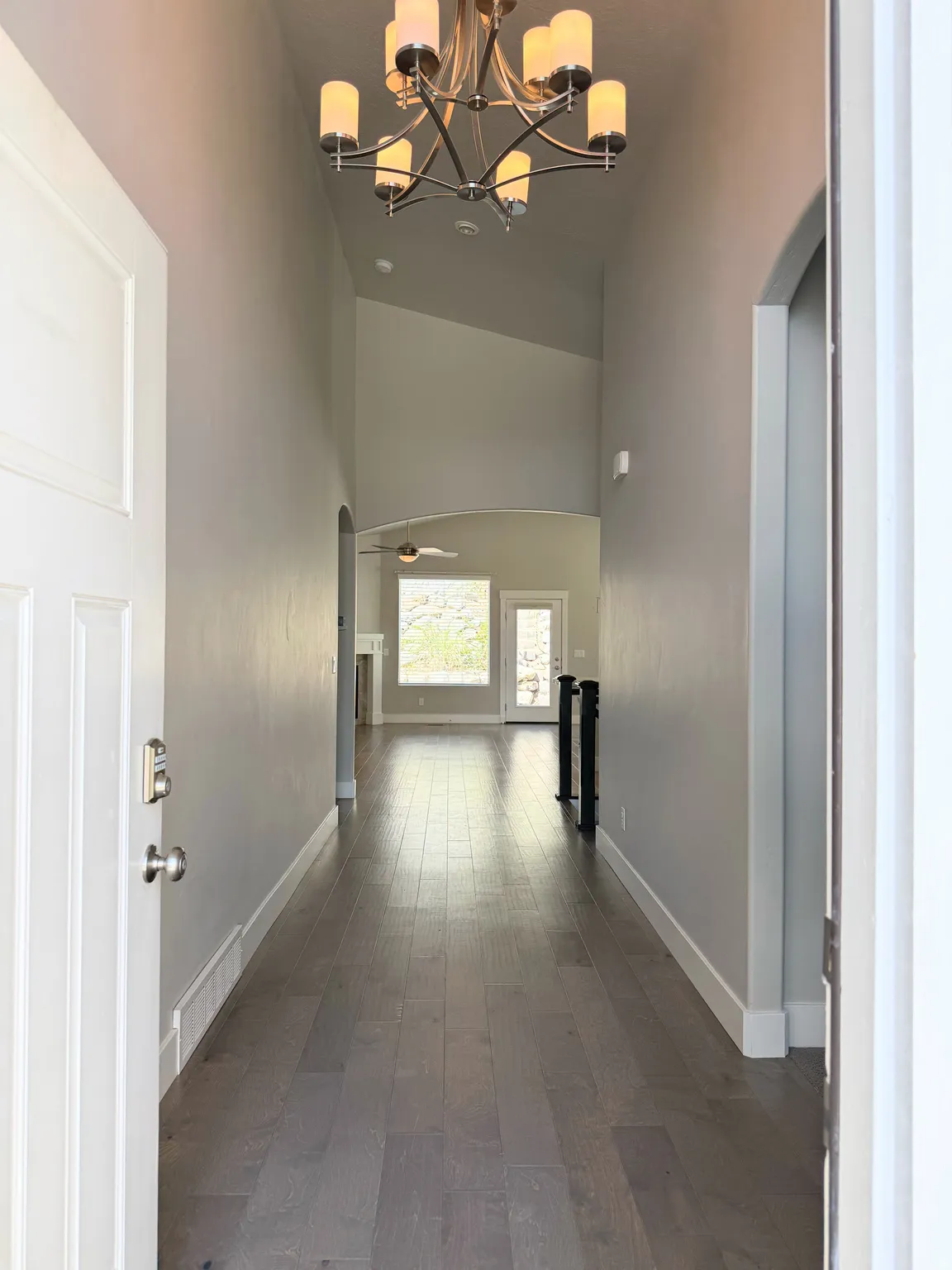 Welcome Home to a vaulted entry foyer with a contemporary chandelier, wood-finish flooring, and arched doorways