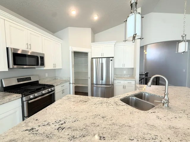 Kitchen featuring light-toned granite countertops, stainless steel appliances, white cabinetry, a double basin sink with a gooseneck faucet, and recessed lighting