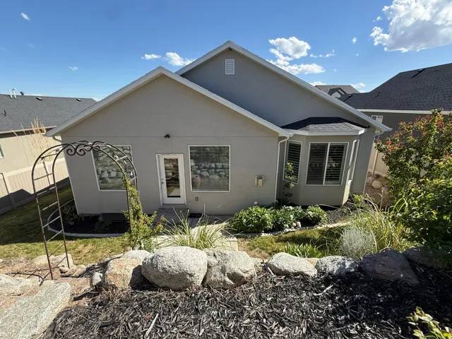 Rear exterior featuring a stucco facade, multiple windows, and a glass-paneled door, and and iron ornamental trellis garden arch.