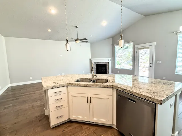 Kitchen island featuring a double-basin sink, stainless steel dishwasher, and stone-finish countertop