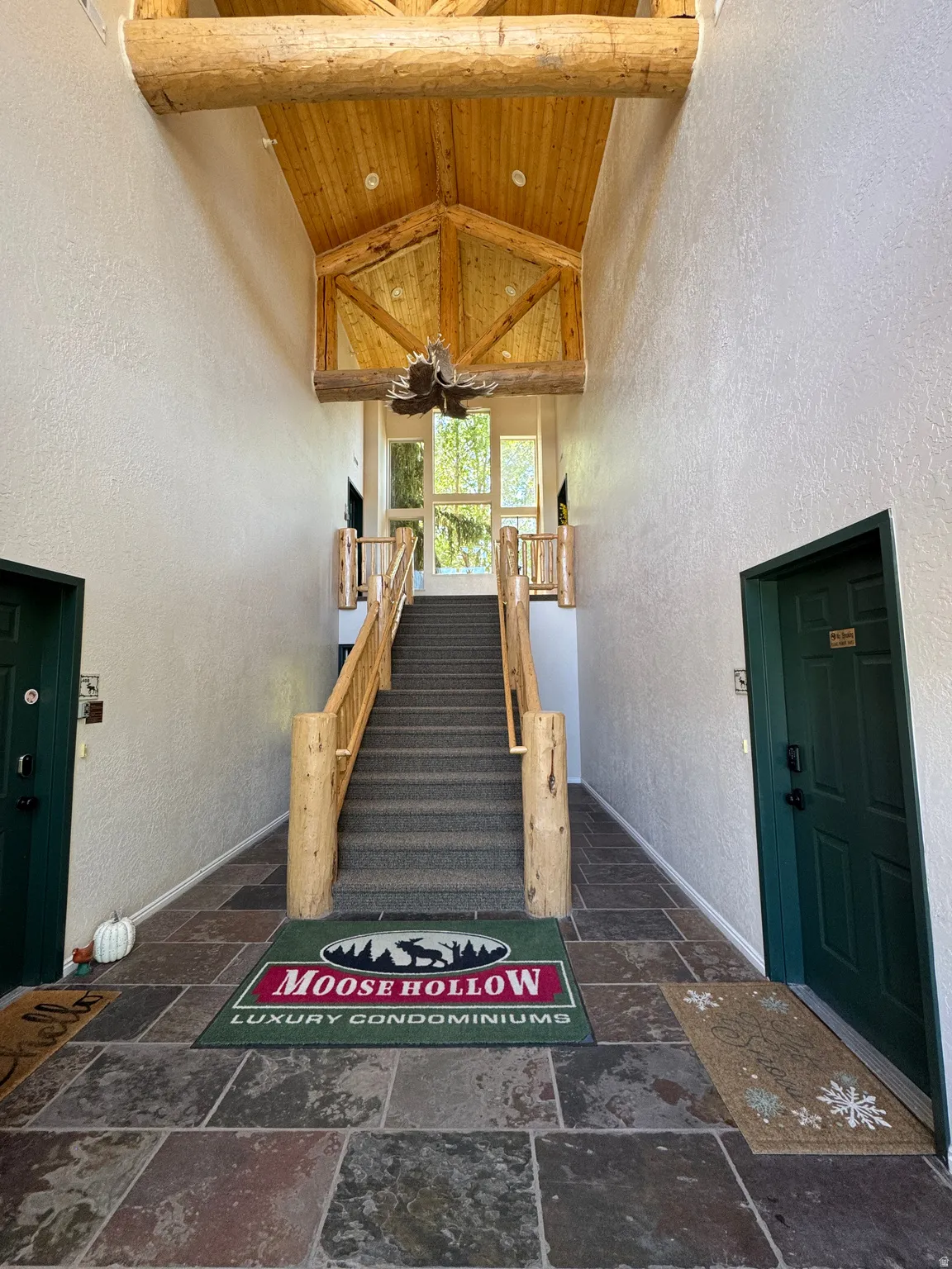 Vaulted ceiling with exposed log beams, a chandelier and stairs to the upstairs condos. This area is maintained by the HOA. Owners storage closet is a locked unit to the left under upstairs landing space