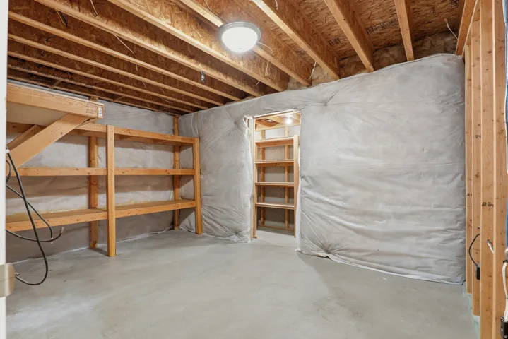 Unfinished basement featuring exposed wood joists, concrete flooring, and pre-built wooden shelving