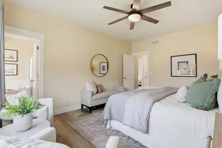 Spacious interior room featuring wood-finish flooring, a contemporary ceiling fan with integrated lighting, and a doorway opening to an additional room with a white soaking tub