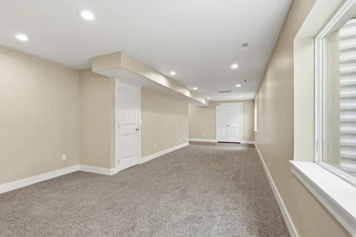 Spacious finished room featuring neutral carpet, light neutral wall paint, recessed lighting, white baseboards, and a window with a white frame