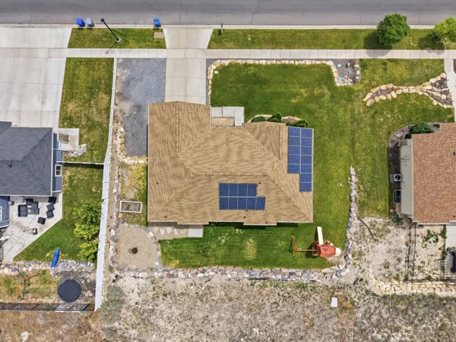 Residential property featuring a brown shingle roof, integrated solar panels, a concrete driveway, and expansive green lawn areas