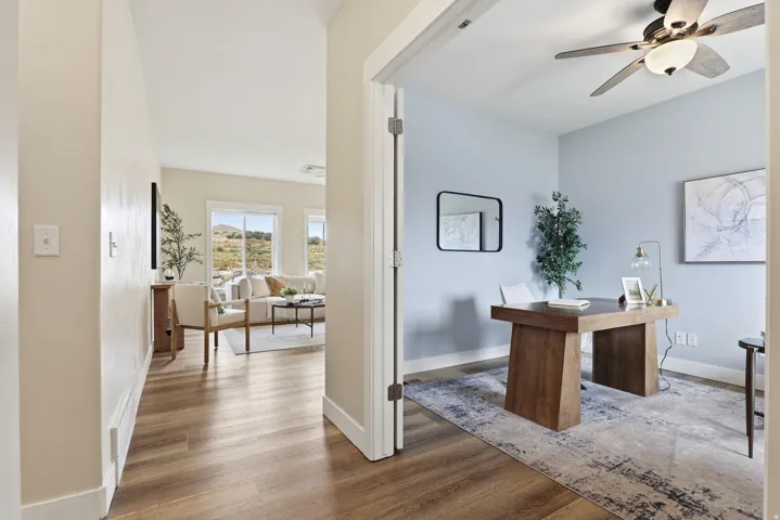 Dedicated office space featuring light blue walls, a ceiling fan with integrated lighting, and wood-finish flooring