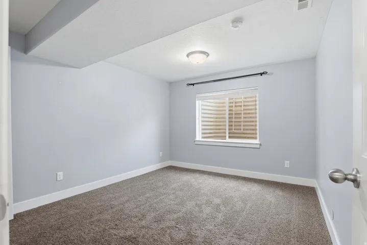 Carpeted room with a ceiling-mounted light fixture, a window with horizontal blinds, and a white door featuring a brushed nickel knob
