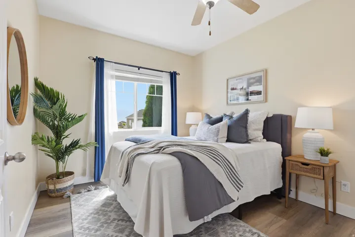 Bedroom featuring a window with blue curtains, wood-finish flooring, a ceiling fan, and light-toned walls