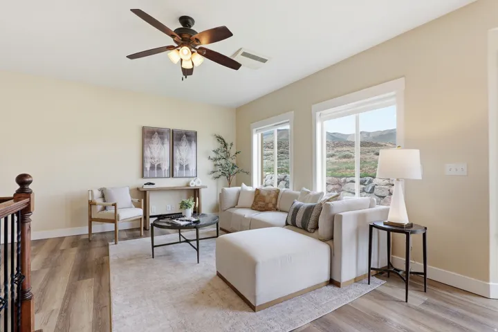 Spacious living area featuring wood-finish flooring, light neutral wall tones, and a ceiling fan with integrated lighting