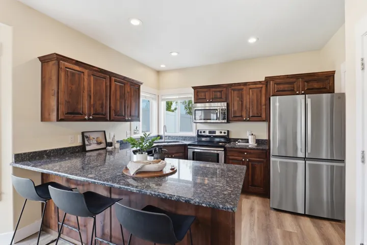 Kitchen featuring a central island with a stone countertop, rich wood cabinetry, stainless steel appliances, recessed lighting, and wood-finish flooring