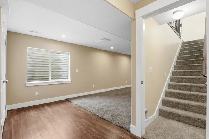 Carpeted staircase leading to an open finished area featuring recessed lighting, a window with horizontal blinds, and wood-finish flooring
