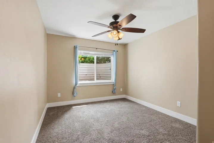 Neutral tone walls with white trim, brown textured carpet, and a ceiling fan with integrated lighting