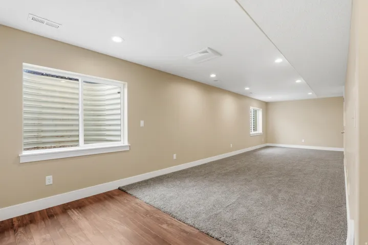 Spacious room featuring recessed lighting, a combination of wood-finish flooring and plush carpeting, multiple windows with white trim, and neutral-toned walls