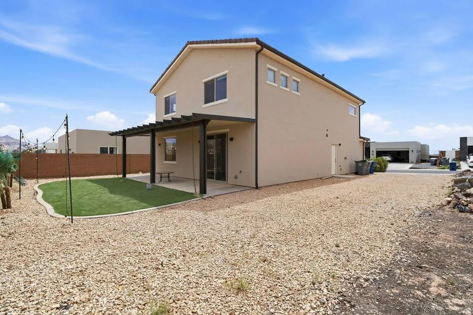 Rear exterior featuring a covered patio with dark pergola, artificial turf, and extensive gravel landscaping