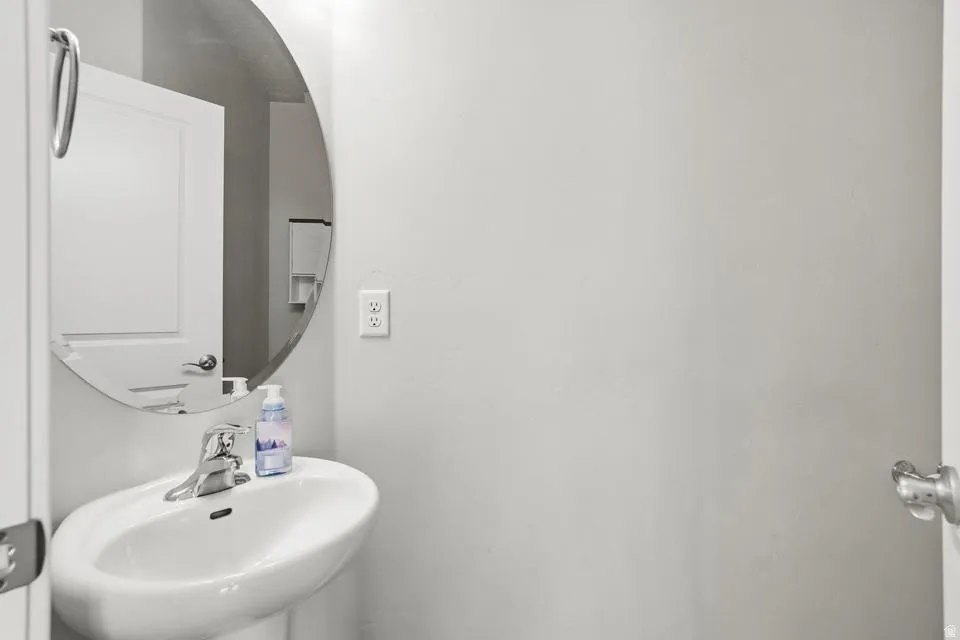 Pedestal sink with a chrome faucet, round wall mirror, and neutral wall paint