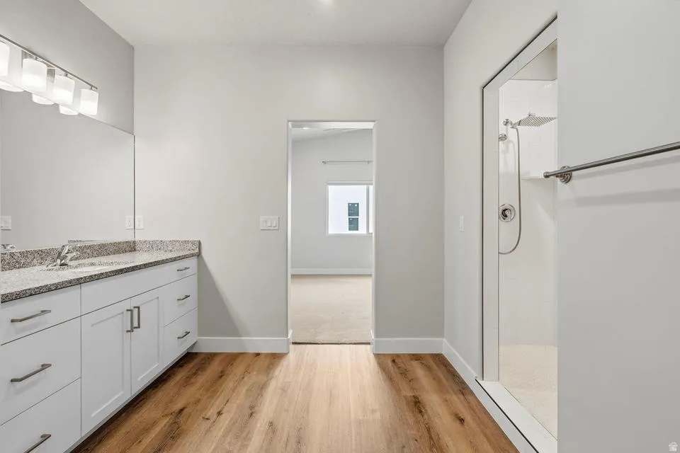 Modern bathroom featuring a double vanity with stone-finish countertop, white cabinetry, and wood-finish flooring