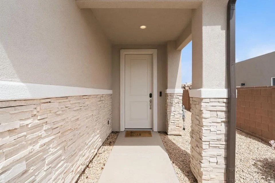 Front entry featuring a solid paneled door, recessed lighting, and stucco exterior with stone veneer accents on columns and lower wall