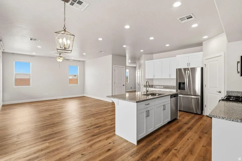 Open-concept living space featuring wood-finish flooring, recessed lighting, a kitchen island with a sink, white cabinetry, and stainless steel appliances