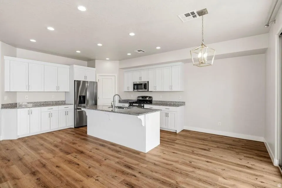 Spacious kitchen featuring an expansive island with an integrated sink, wood-finish flooring, white cabinetry, recessed lighting, and granite countertops