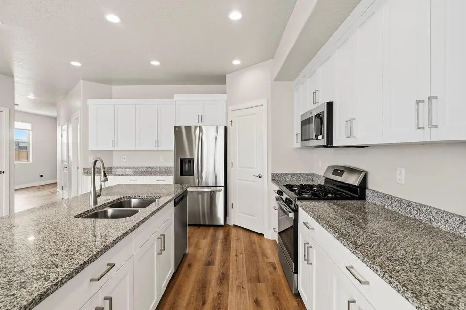 Kitchen featuring white shaker cabinetry, stainless steel appliances, granite countertops, an undermount double basin sink, and wood-finish flooring