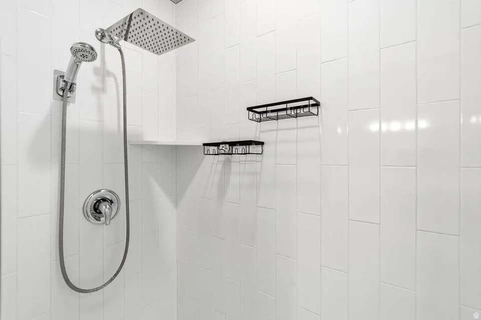 Shower enclosure featuring white subway tile, a rain showerhead, and a handheld shower sprayer