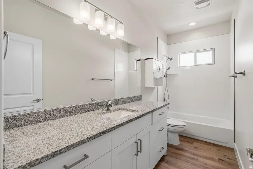 Bathroom featuring a light-toned granite countertop, a single undermount sink with a chrome faucet, and white shaker-style cabinetry with dark hardware