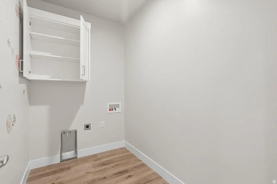 Utility room featuring wood-finish flooring, white baseboards, light gray walls, and a white wall-mounted cabinet with open shelving