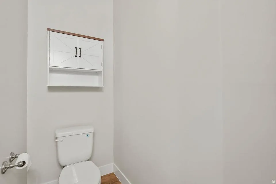 White wall-mounted cabinet with wood-finish top and black hardware, situated above a white toilet