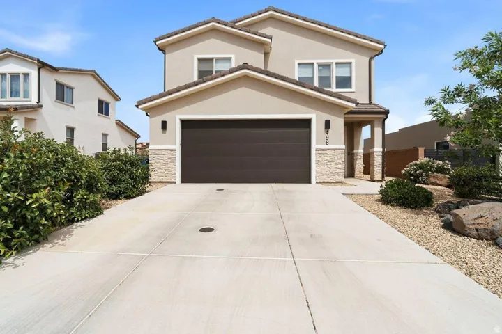 Two-story stucco residence featuring a two-car garage with a brown door, stone accents, and a covered entry