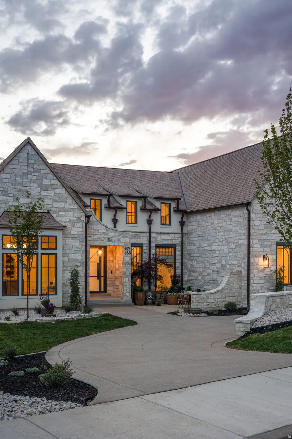 Stone facade residence featuring multiple gables, an arched entryway, and a winding concrete driveway