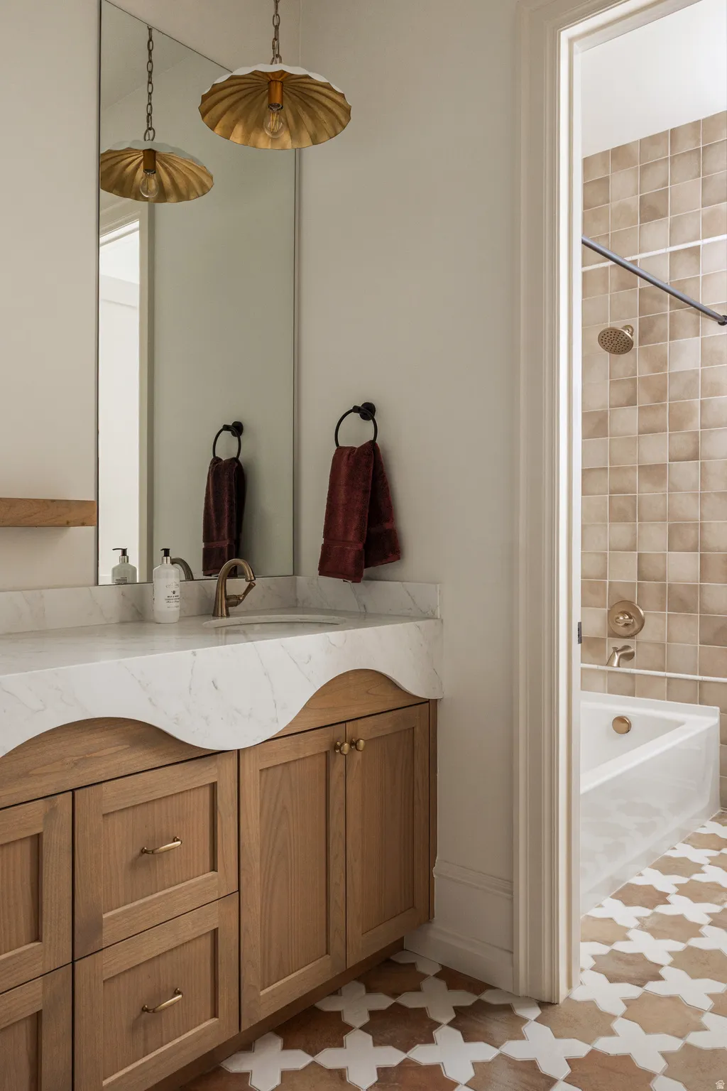 Bathroom vanity featuring a light wood-finish cabinet with brass hardware, a white countertop with an organic edge, and a rectangular undermount sink