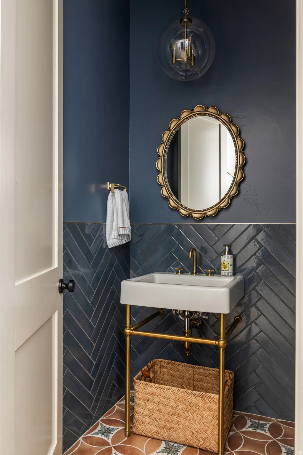 Powder room featuring a ceramic pedestal sink with brass-finish hardware, blue chevron tile wainscoting, and patterned floor tiles