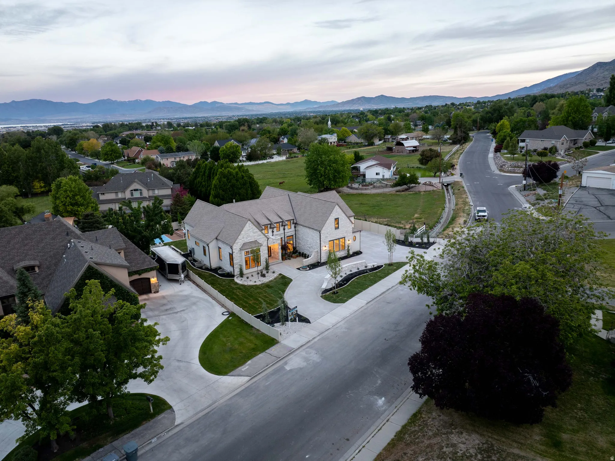 Stately residence featuring a stone and stucco exterior, multi-gabled roofline, expansive concrete driveways, and manicured landscaping
