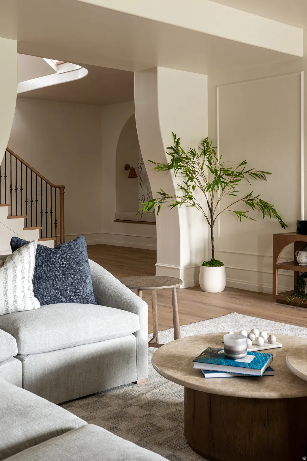 Open-concept living area featuring light wood-finish flooring, a contemporary staircase with dark iron balusters, arched doorways, and elegant wall molding