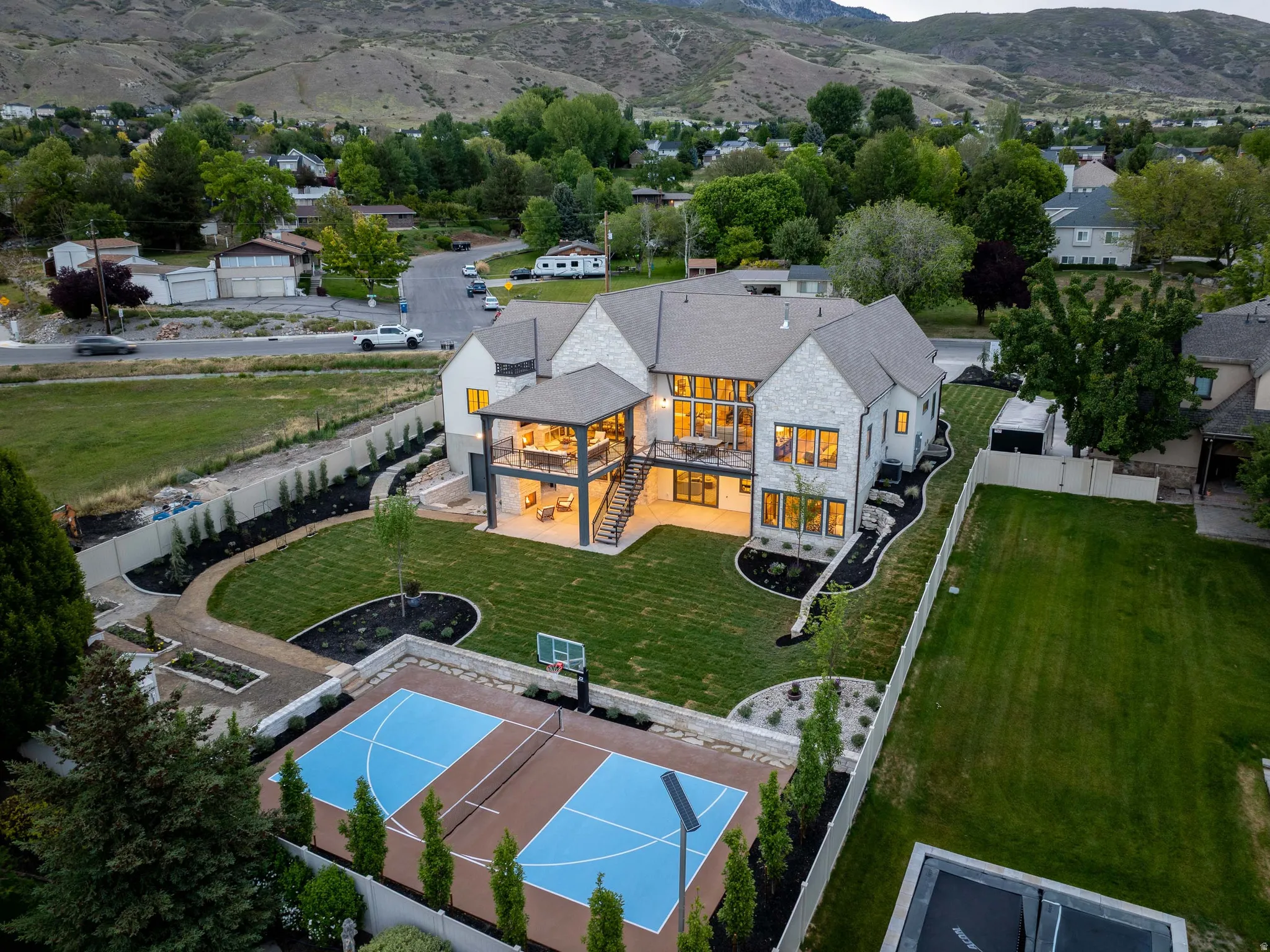 Contemporary stone and siding exterior with multiple decks, extensive landscaping, and a dedicated sports court