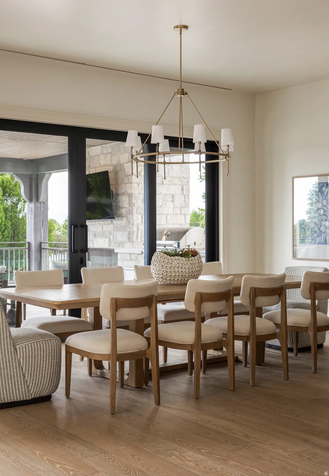 Spacious dining area featuring wood-finish flooring, a contemporary gold-tone chandelier, and sliding glass doors opening to an outdoor living space with stone accents