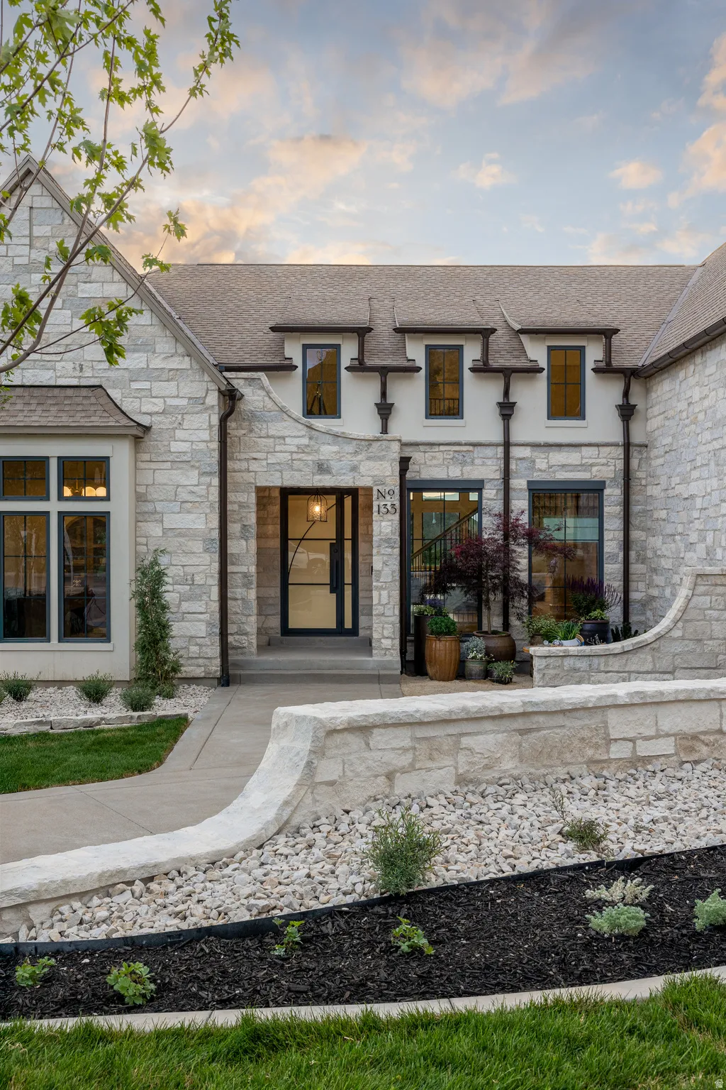 Stone facade residence featuring a prominent arched entry, dark-framed windows, and decorative dormers